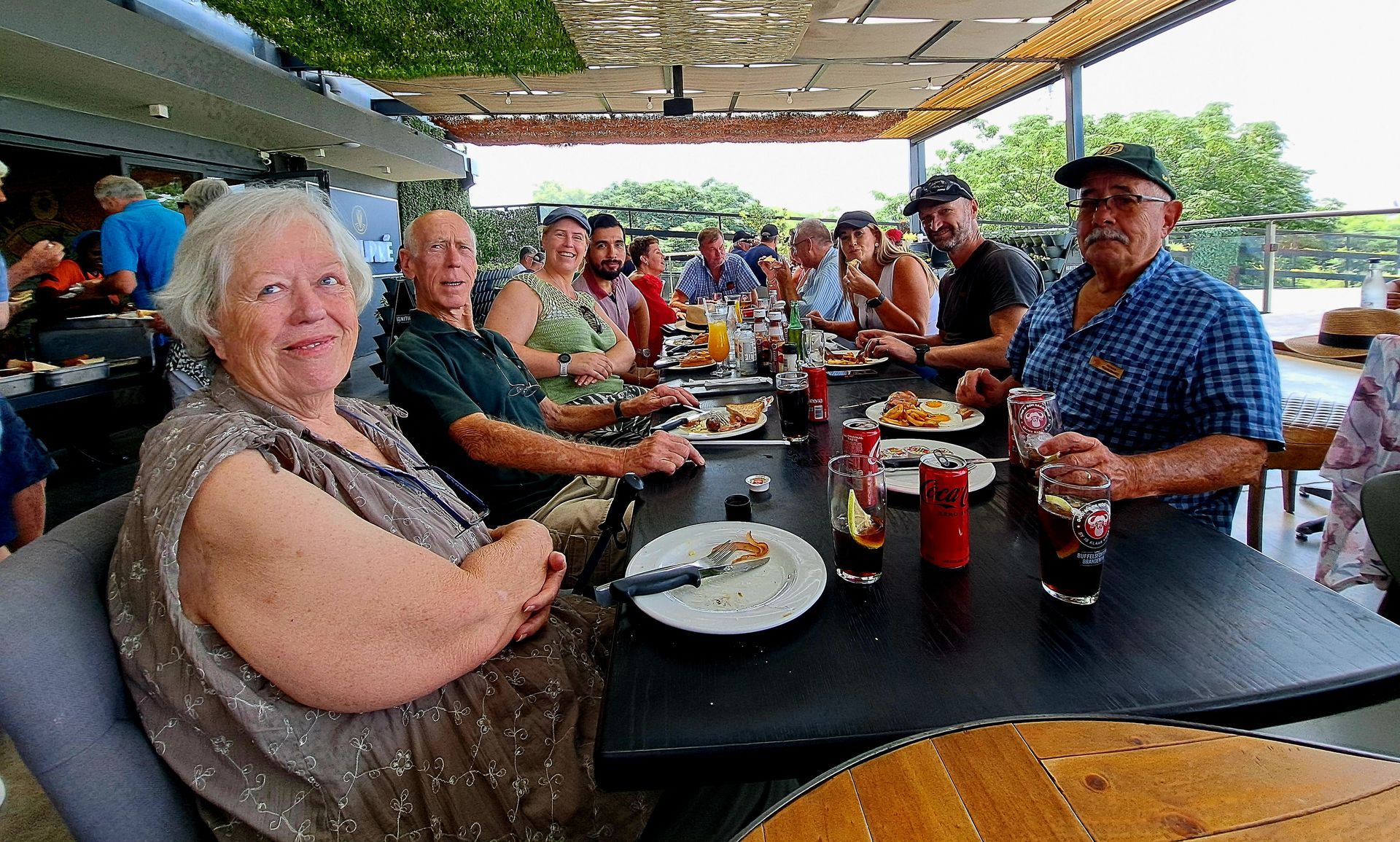 People at an outdoor restaurant table; food, drinks; woman smiling; sunny day.