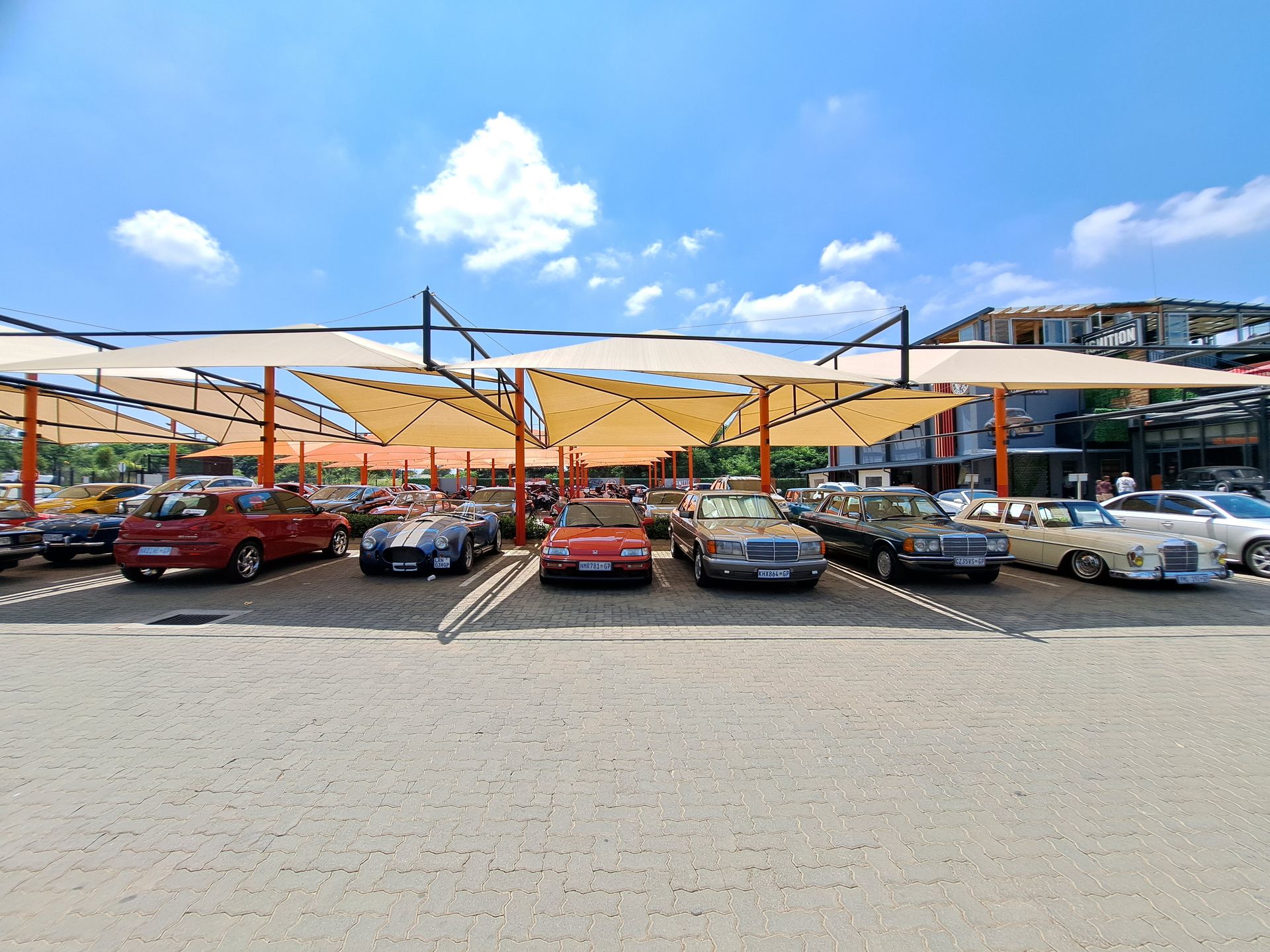 Cars parked under a canopy. Beige covers shade vehicles in an outdoor lot on a sunny day.