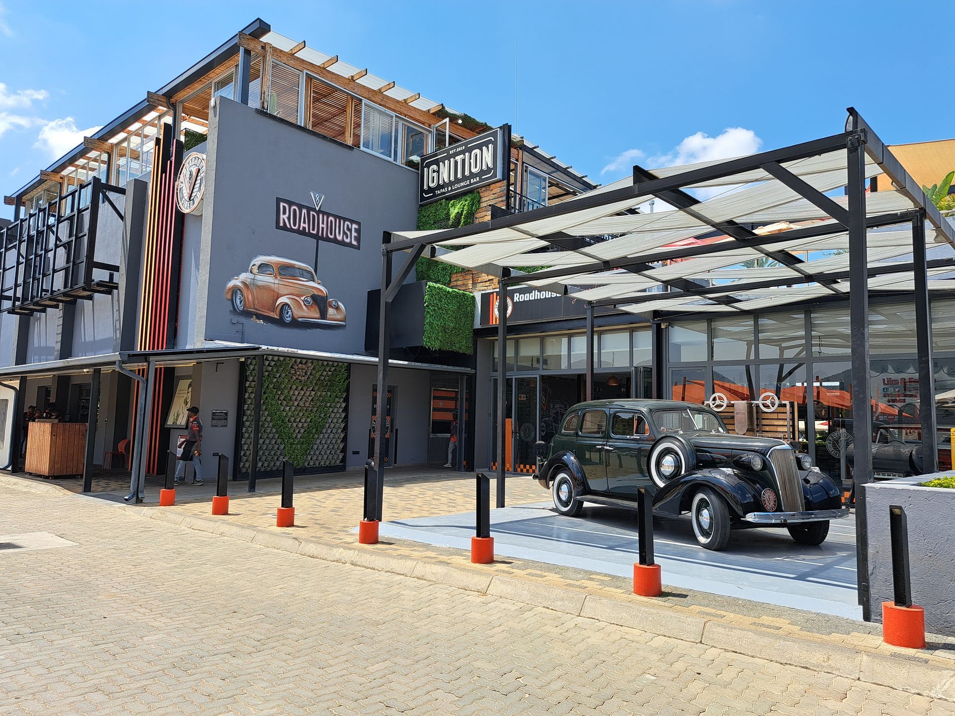 Gray building with vintage car display, featuring a shaded entryway and artificial greenery on the facade.