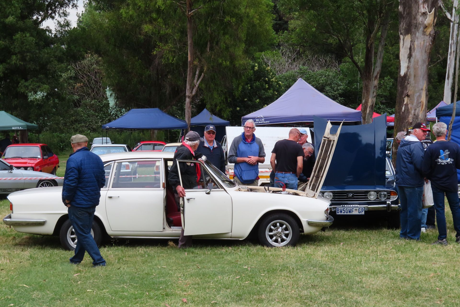 Classic cars on display at an outdoor event with people looking at them.