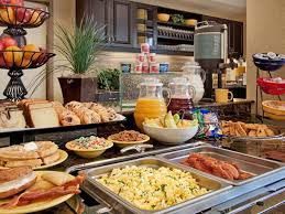Breakfast buffet: assorted foods like eggs, fruits, pastries, and drinks on a counter with trays and bowls.