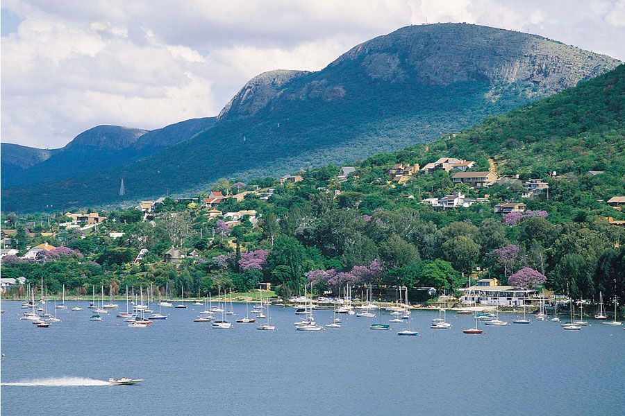 Boats on lake, houses on a green hillside with a mountain backdrop under a blue sky.