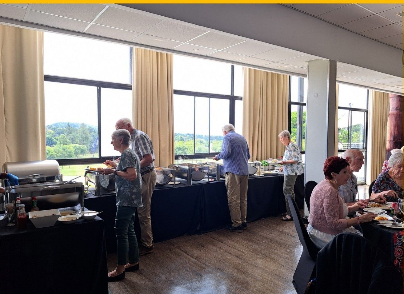 People at a buffet in a room with large windows overlooking a green landscape.
