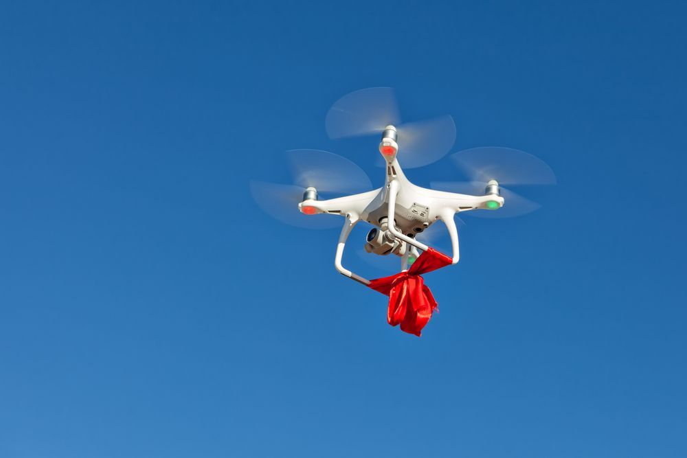 White Drone Carrying a Red Package Against a Clear, Blue Sky — Jetstream Aerial Services in Te Kowai, QLD