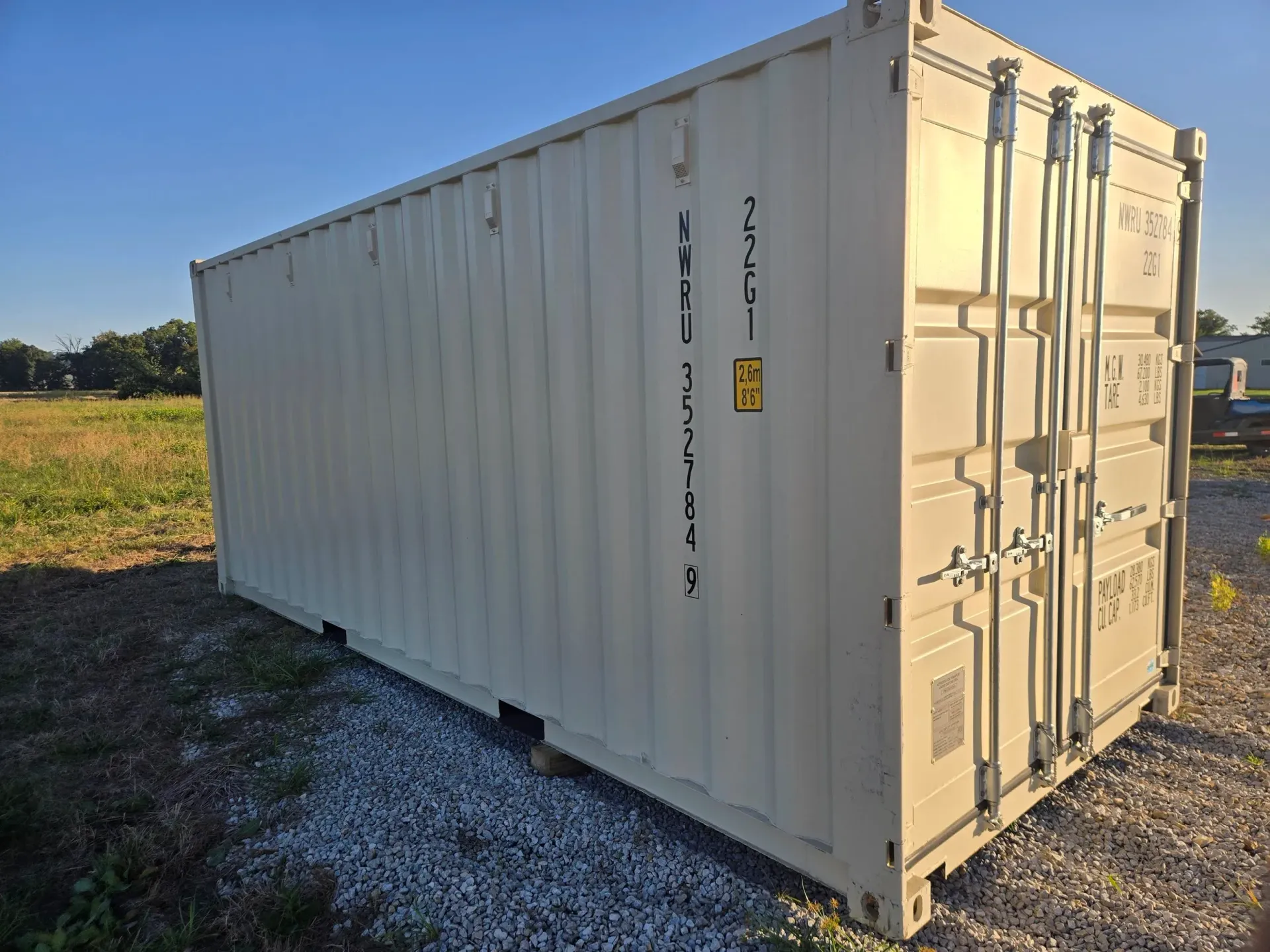 Tan shipping container on gravel in a field with blue sky.