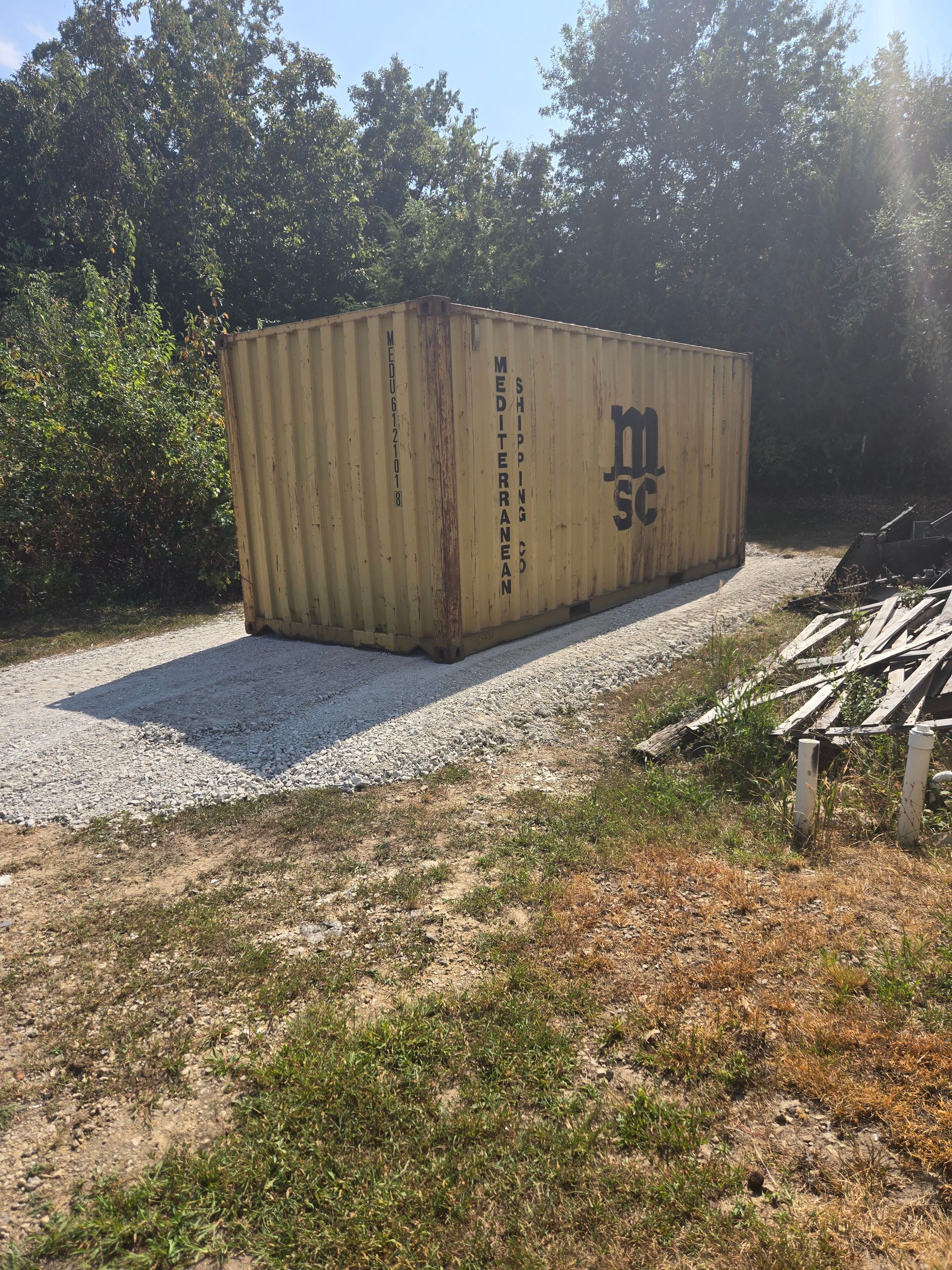 Yellow shipping container on a gravel base, in a wooded area. The container has MSC logo on the side.