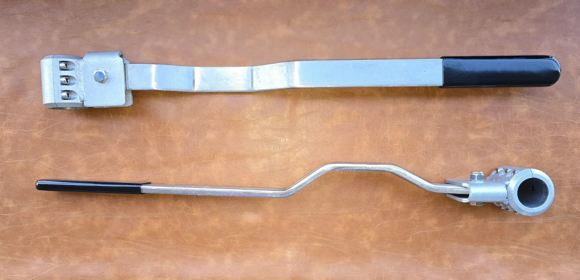 Two metal tools with black handles, one straight, one curved, on a brown surface.