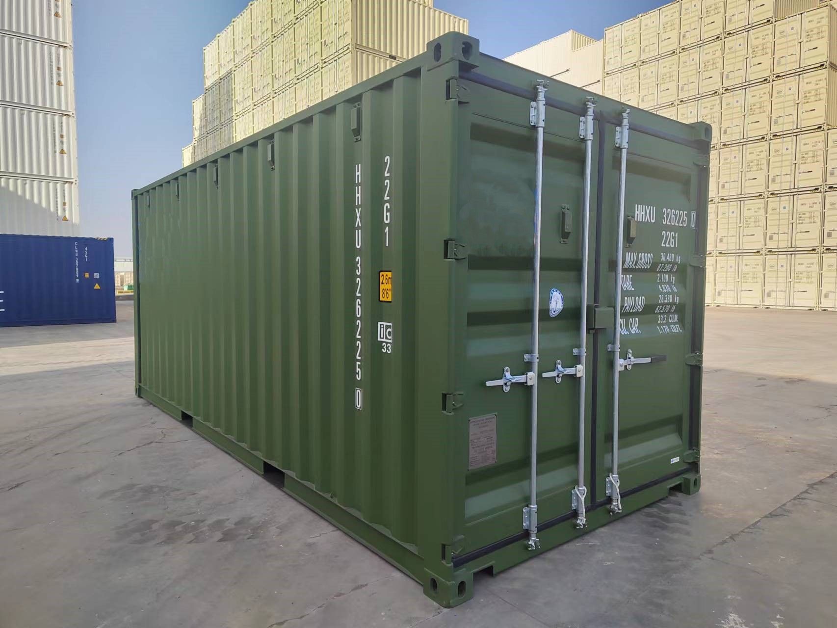 Green shipping container in a yard with other containers.