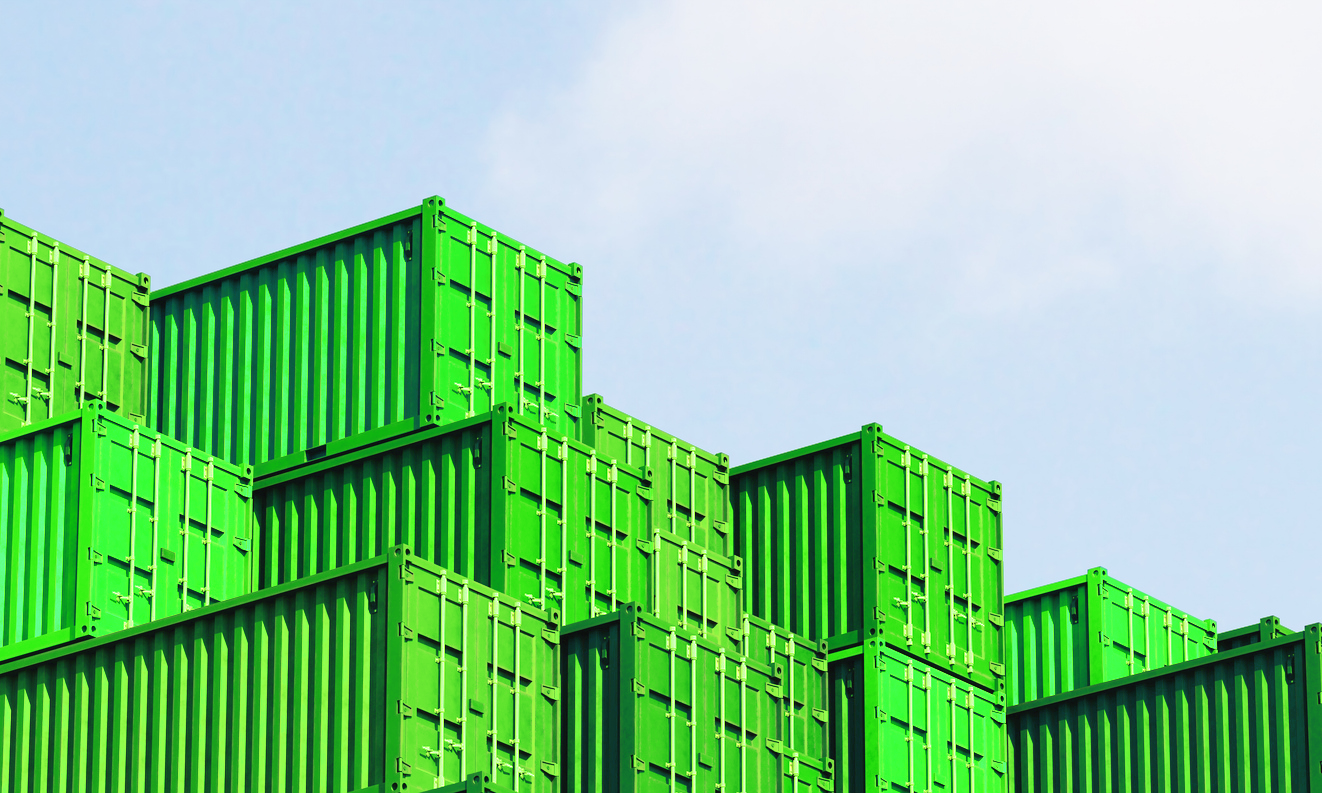 Green shipping containers stacked, against a light blue sky.