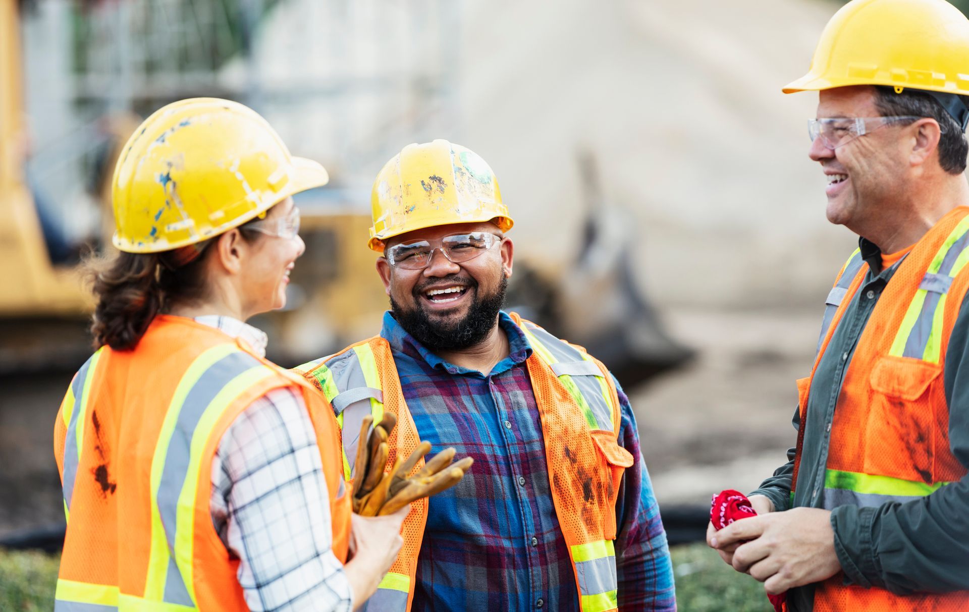 Construction workers in safety vests and helmets talking at job site.