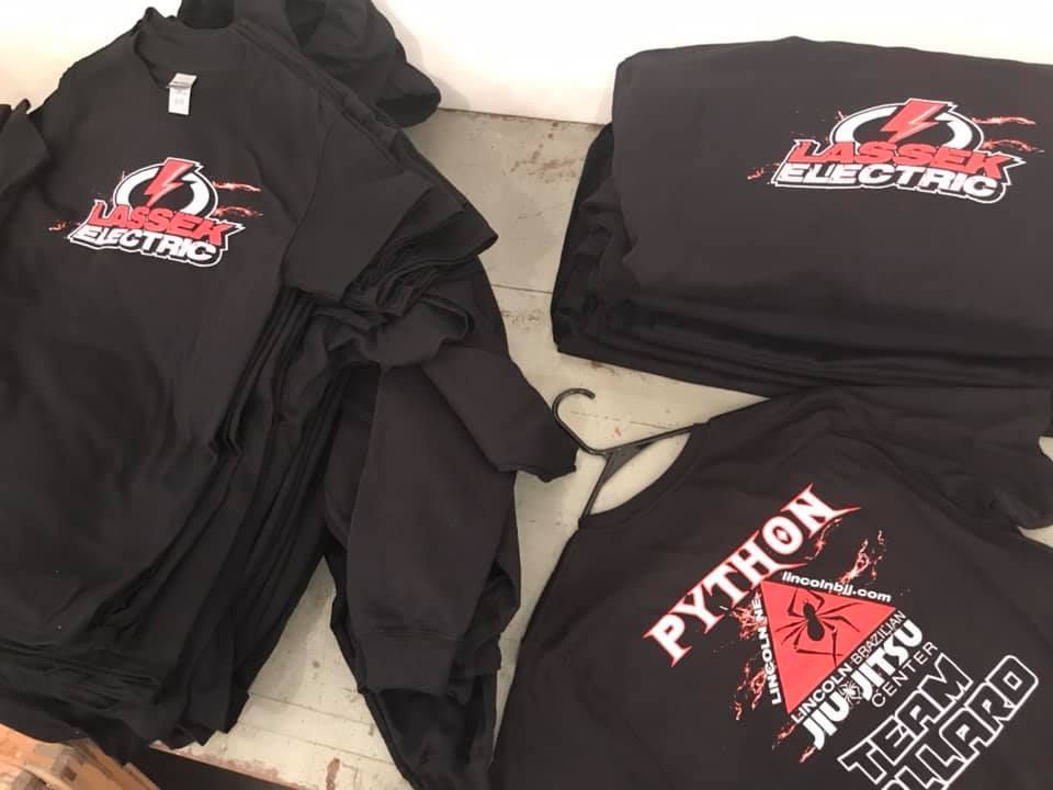 Stacks of black t-shirts printed with company logos, including