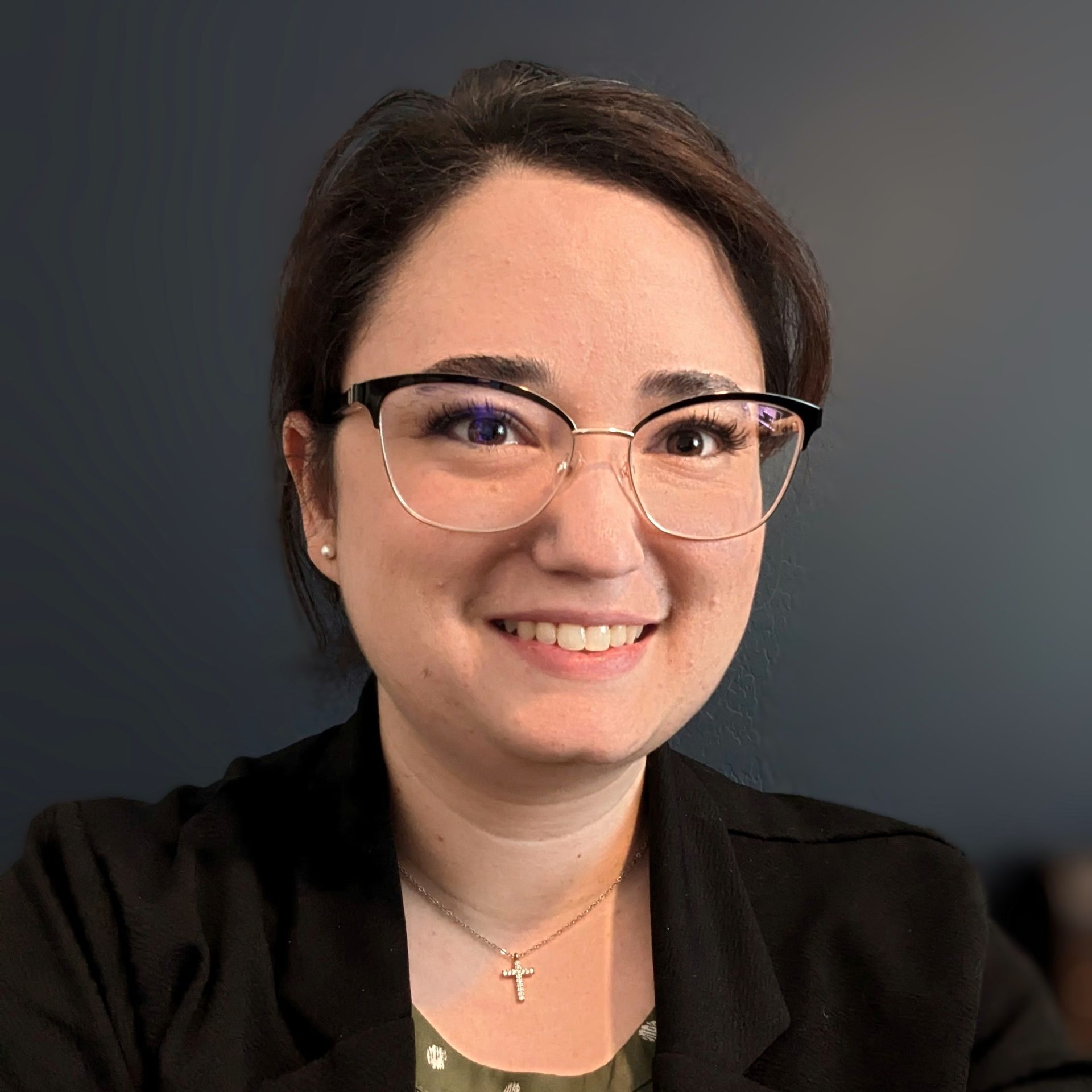 A woman wearing glasses and a cross necklace is smiling for the camera.