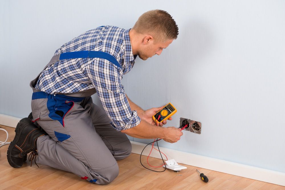 A Man Is Kneeling Down While Using A Multimeter To Test An Electrical Outlet — PRO Solar & Electrical In Port Stephens, NSW
