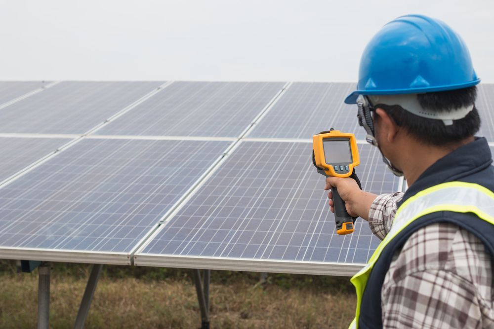 A Man Is Holding A Thermometer In Front Of A Solar Panel — PRO Solar & Electrical In Port Stephens, NSW