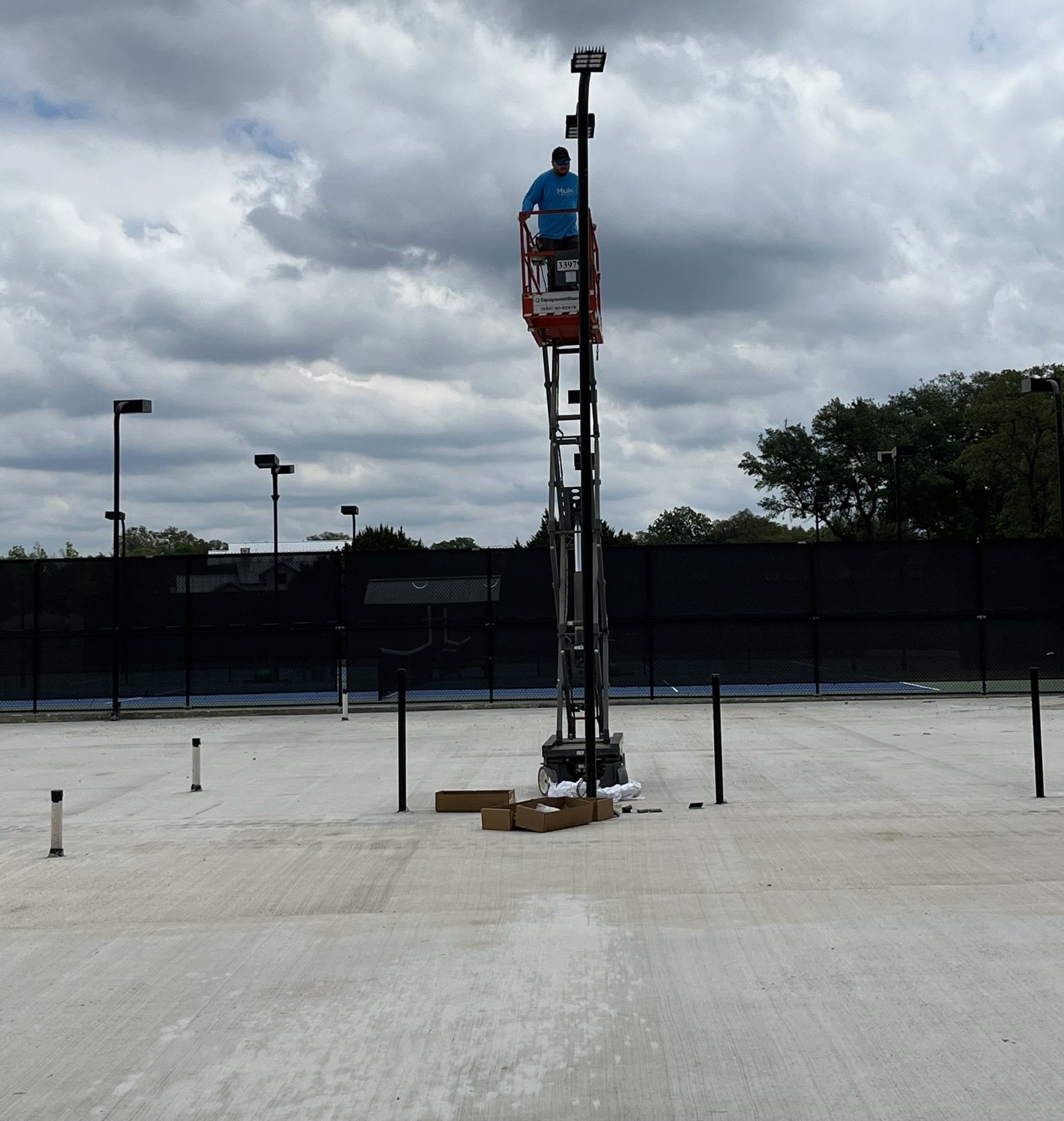 A man in a blue shirt is standing in a bucket on top of a pole