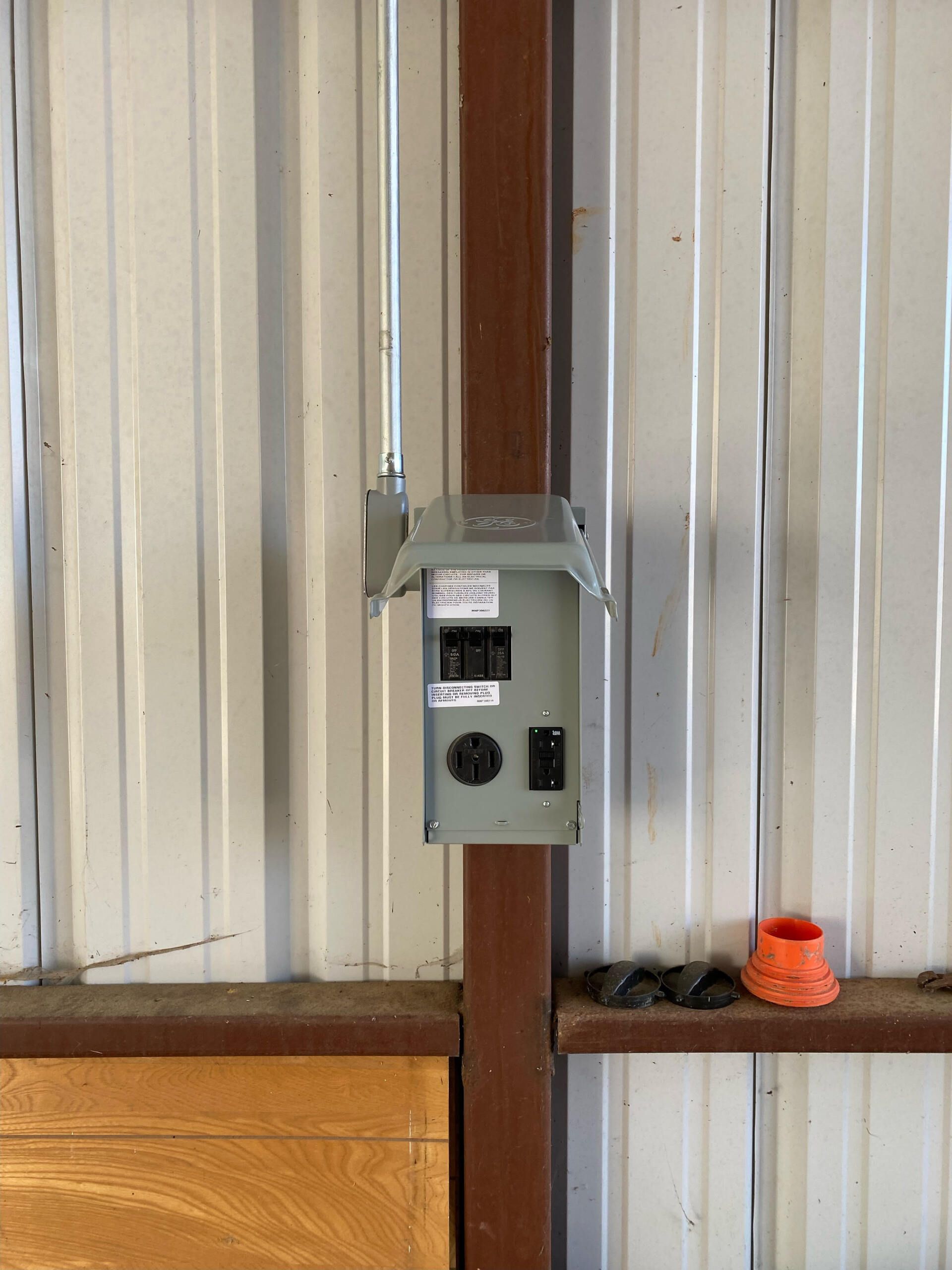 A electrical box is attached to a metal wall in a garage.