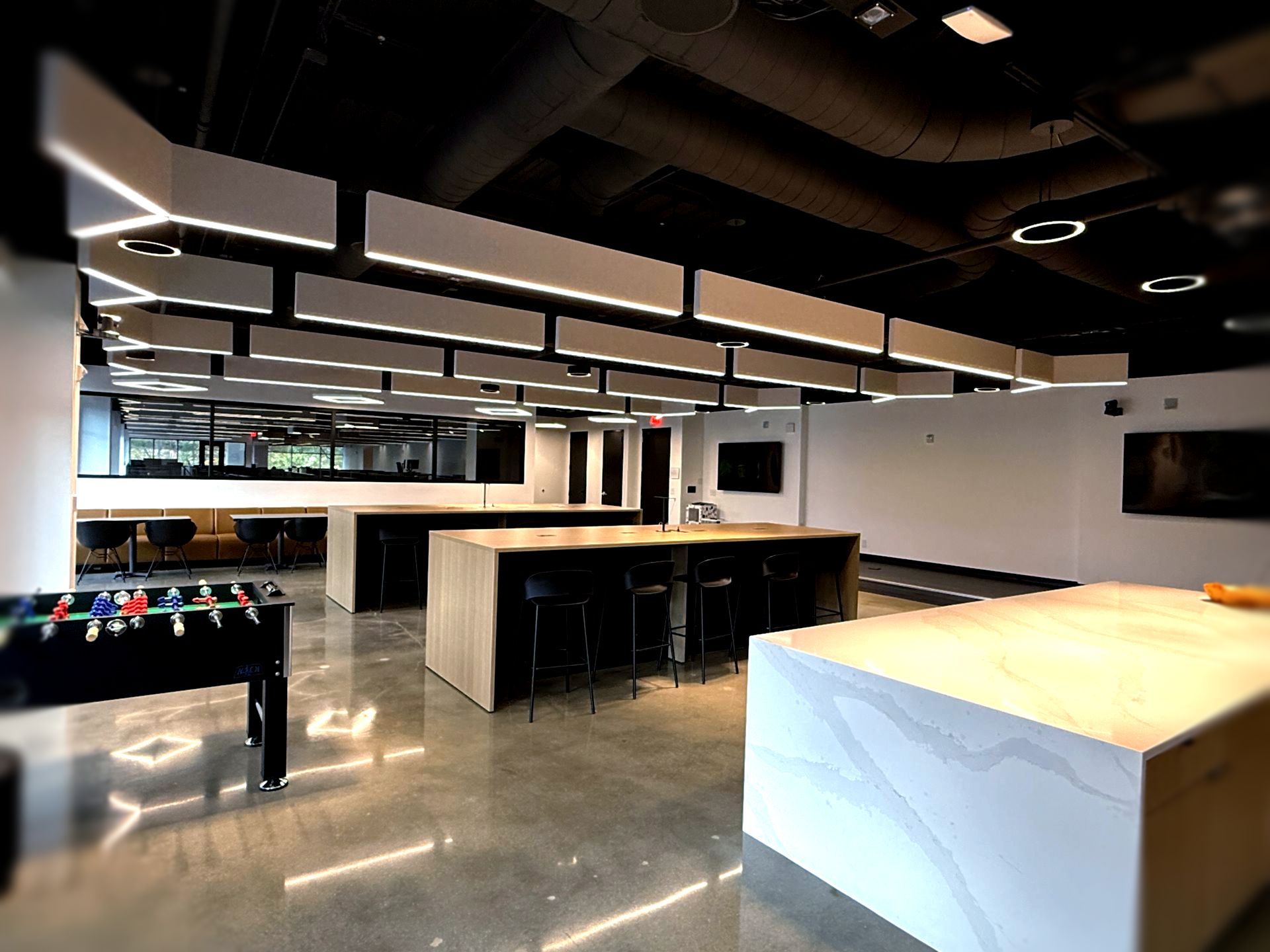 Modern office space with a foosball table, several large work islands with seating, and linear lighting.
