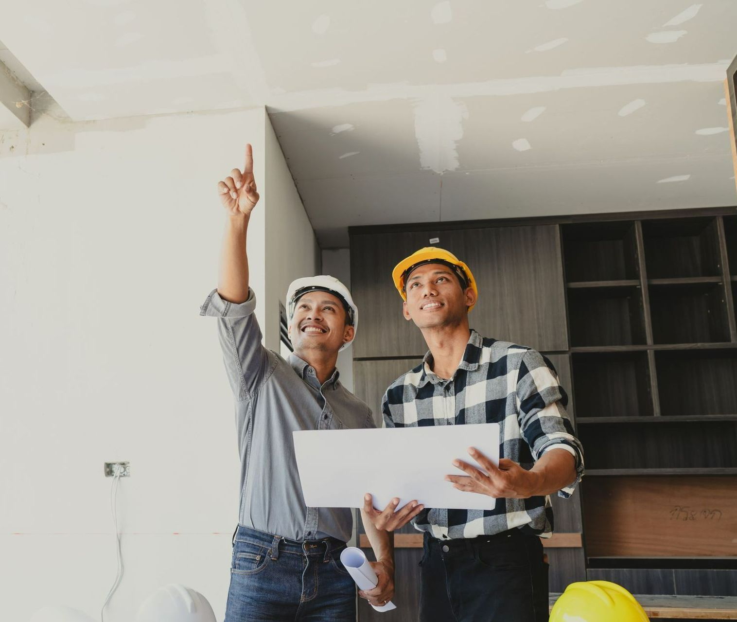 Two Men Wearing Hard Hats Are Looking Up At The Ceiling