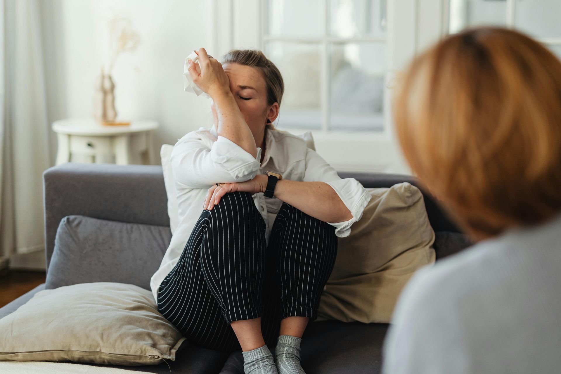 A person sits on a sofa, hand to their forehead, appearing distressed during a counseling session.