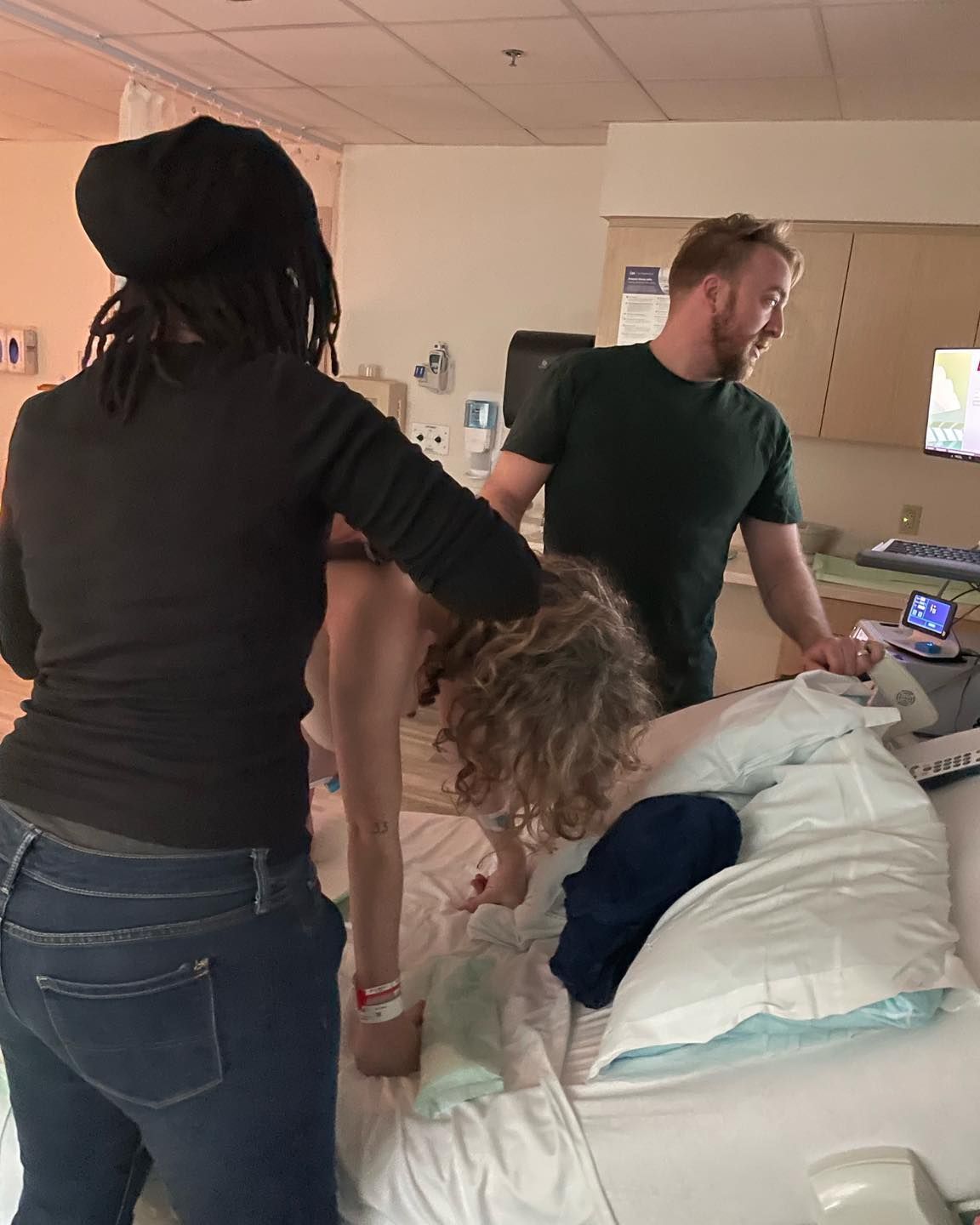 Woman in labor supported by two people in a hospital room.