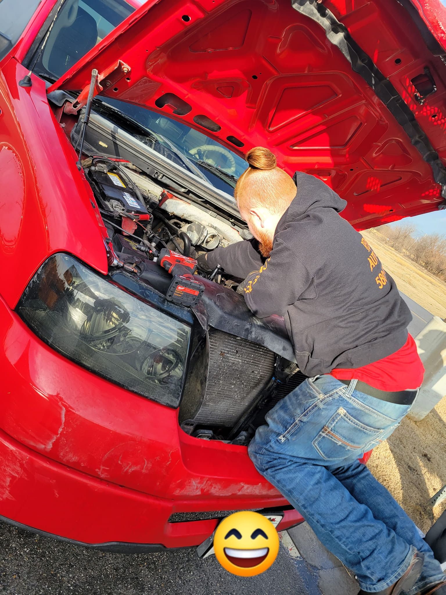 A man is working on the engine of a red car.