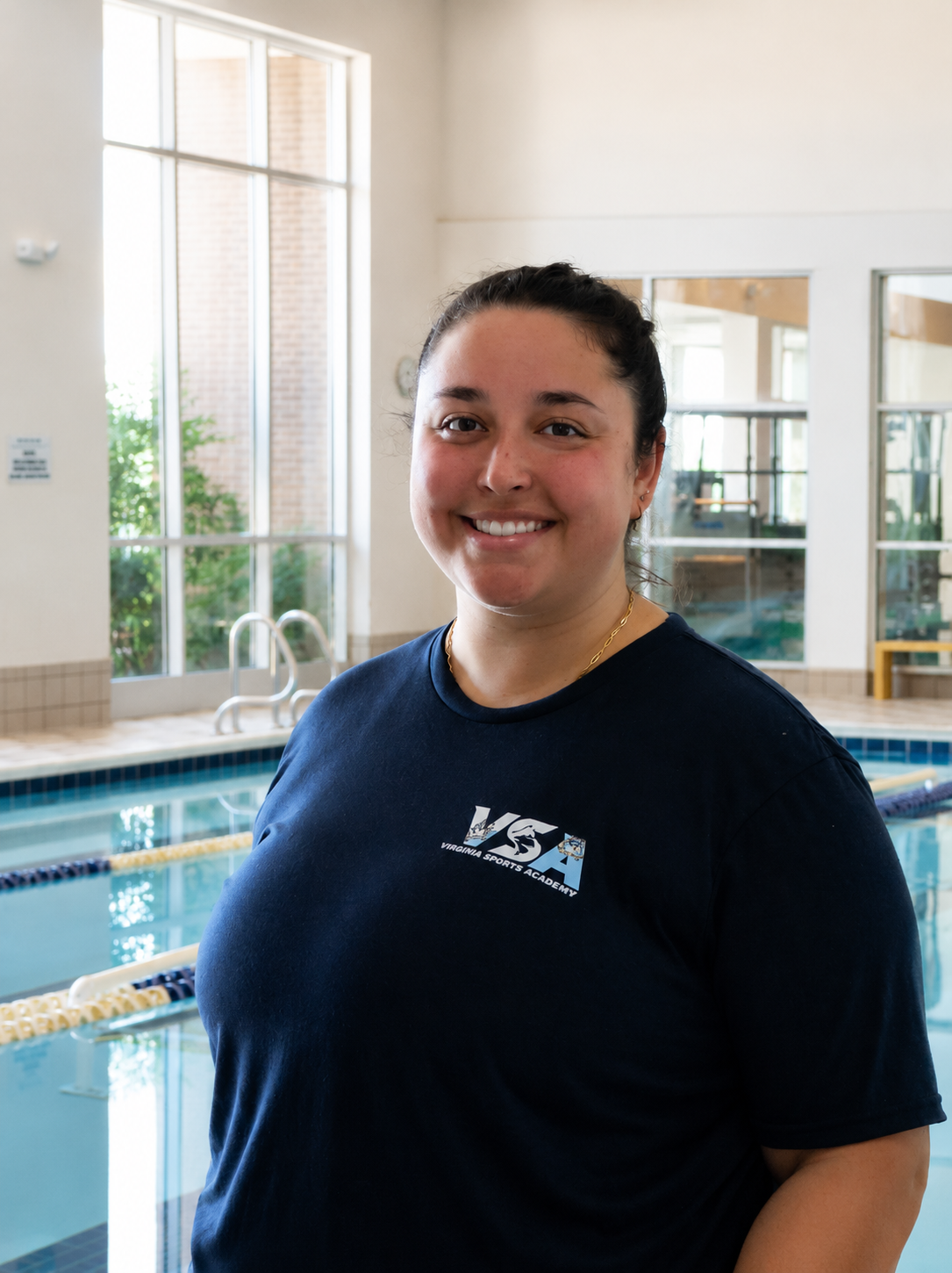 Smiling person in a navy shirt standing by an indoor pool