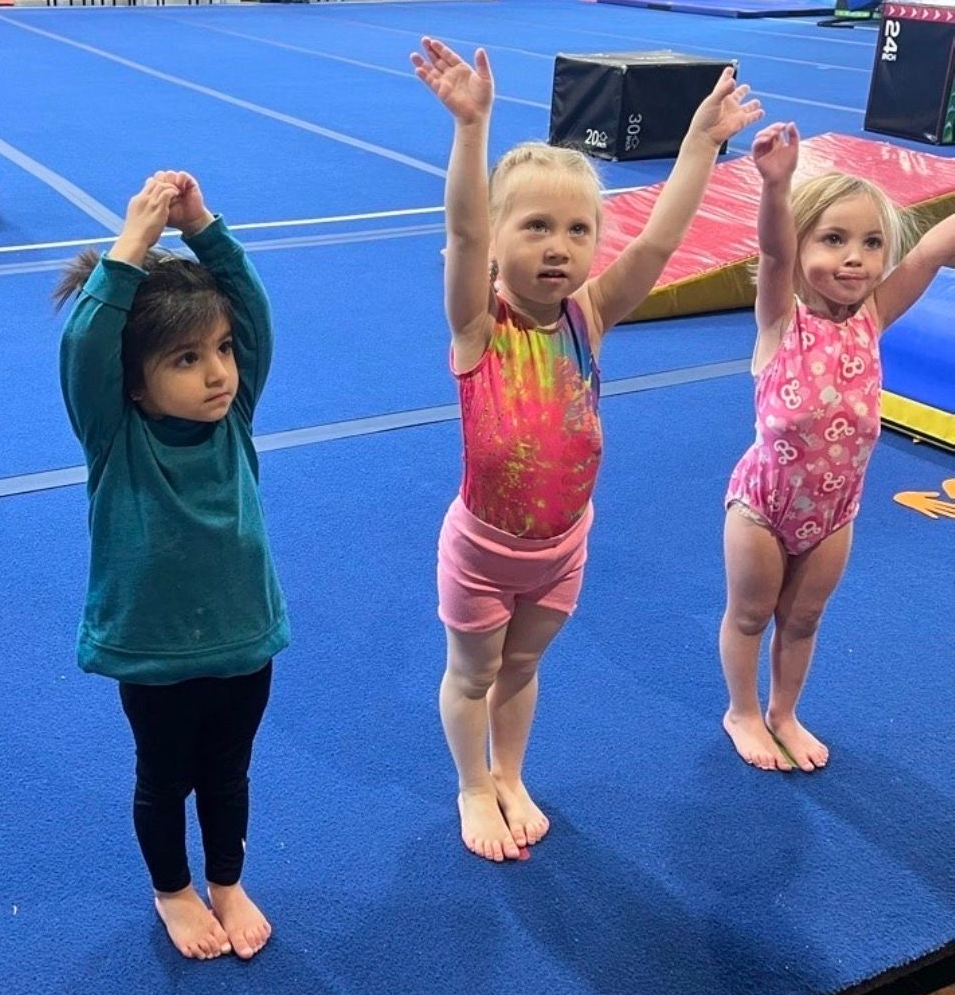 A little girl is doing a split on a blue mat
