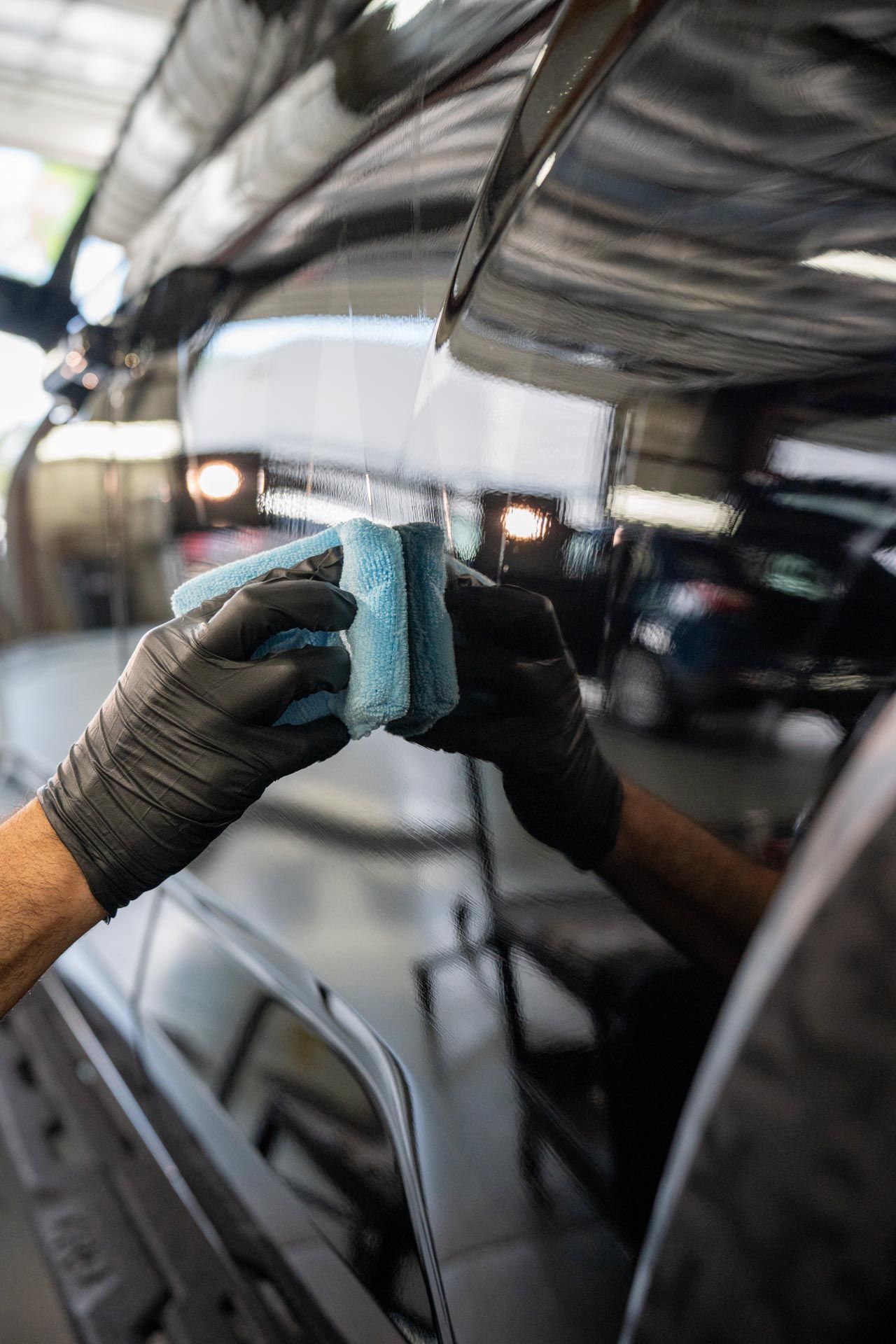 Person in black gloves applying a blue coating with a sponge to a black car.