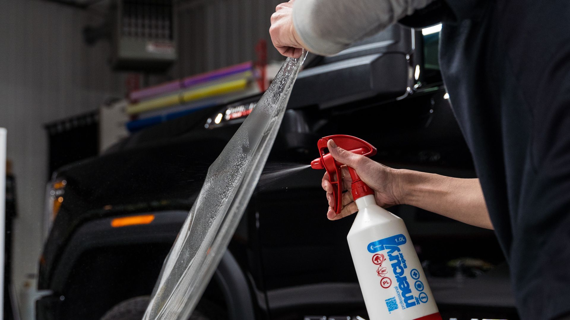 Person sprays window tint film while working on a black truck in a garage.