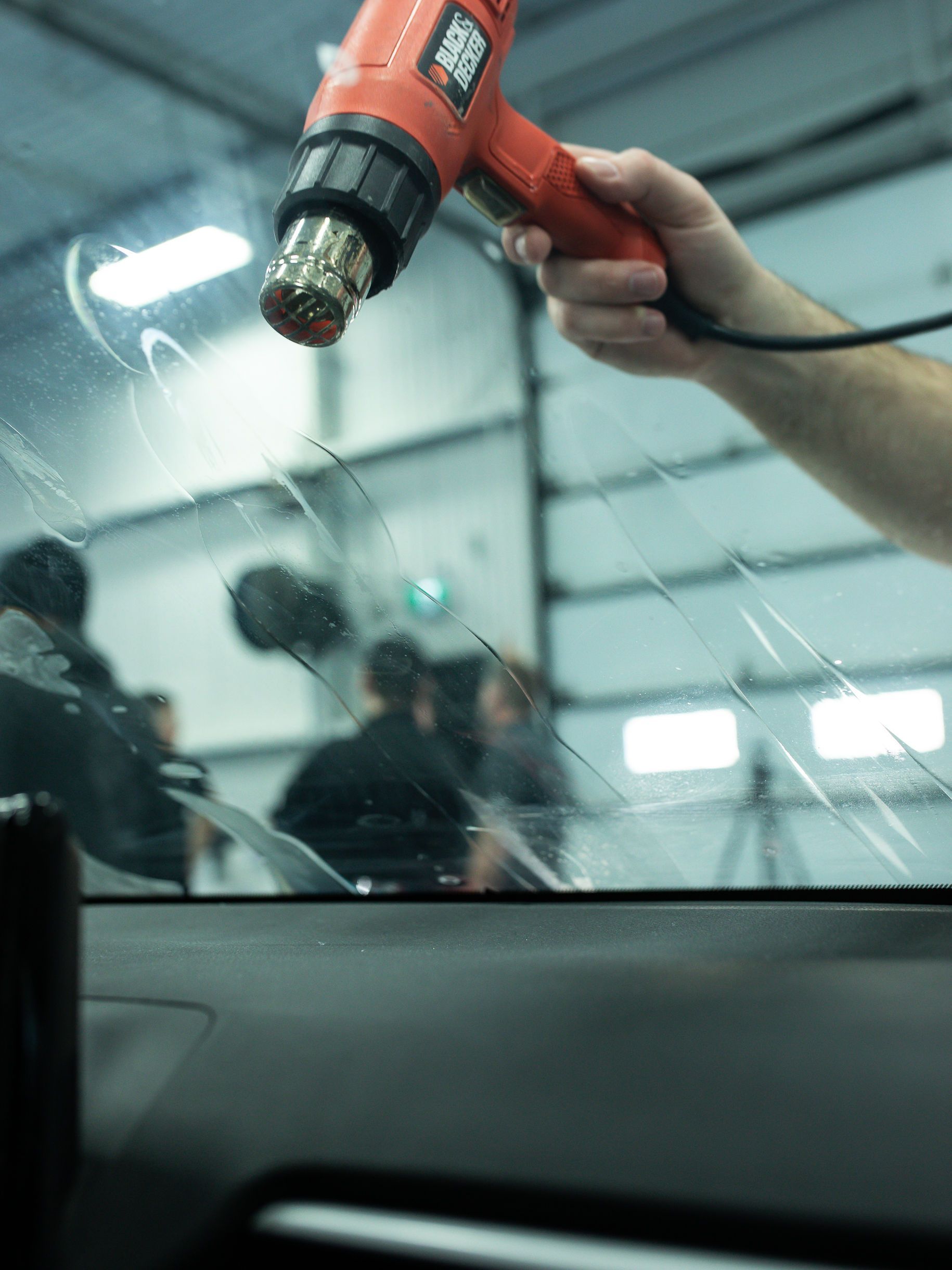 Person applying tint to a car window with a squeegee in a yellow car.
