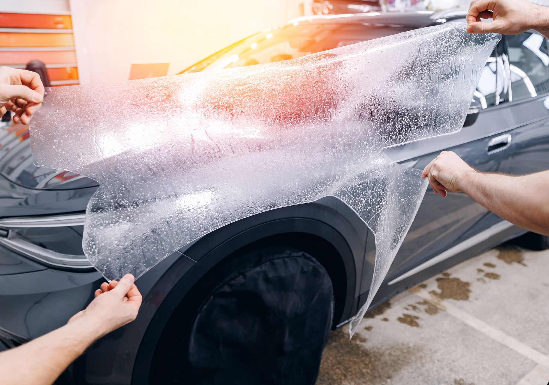 Car hood covered in protective film, in a shop setting, with a person in the background.