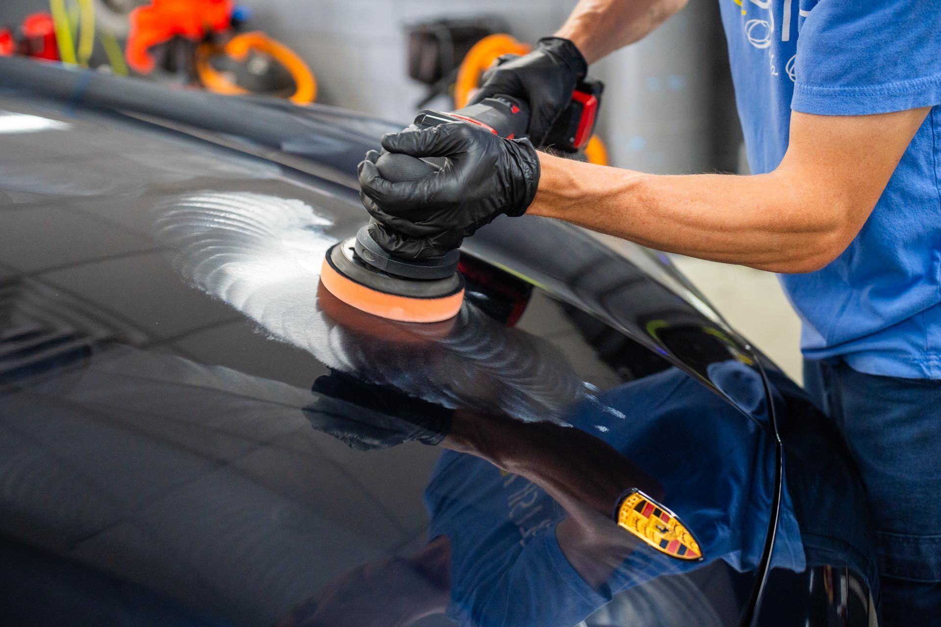 Person in black gloves using a polisher on a dark blue car.
