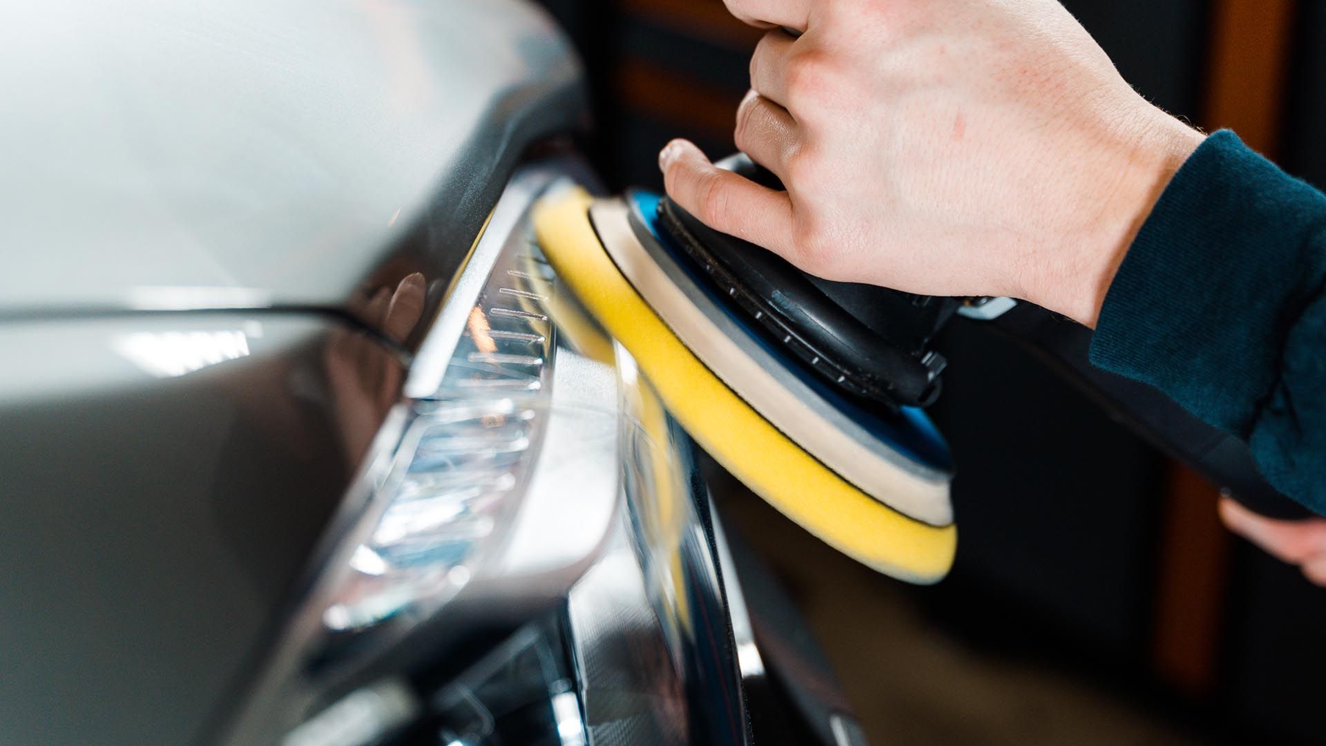 Person polishing a car headlight with a yellow and black buffer.