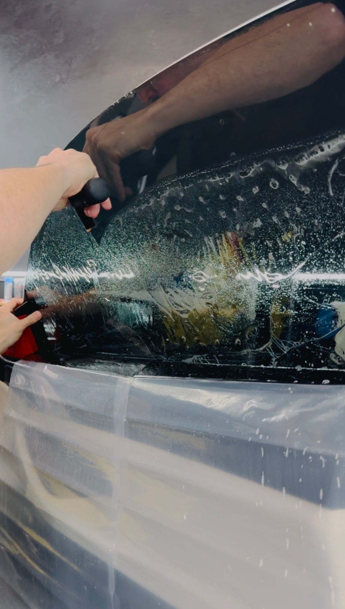 Person applying window tint to a car window, using a squeegee to remove bubbles.