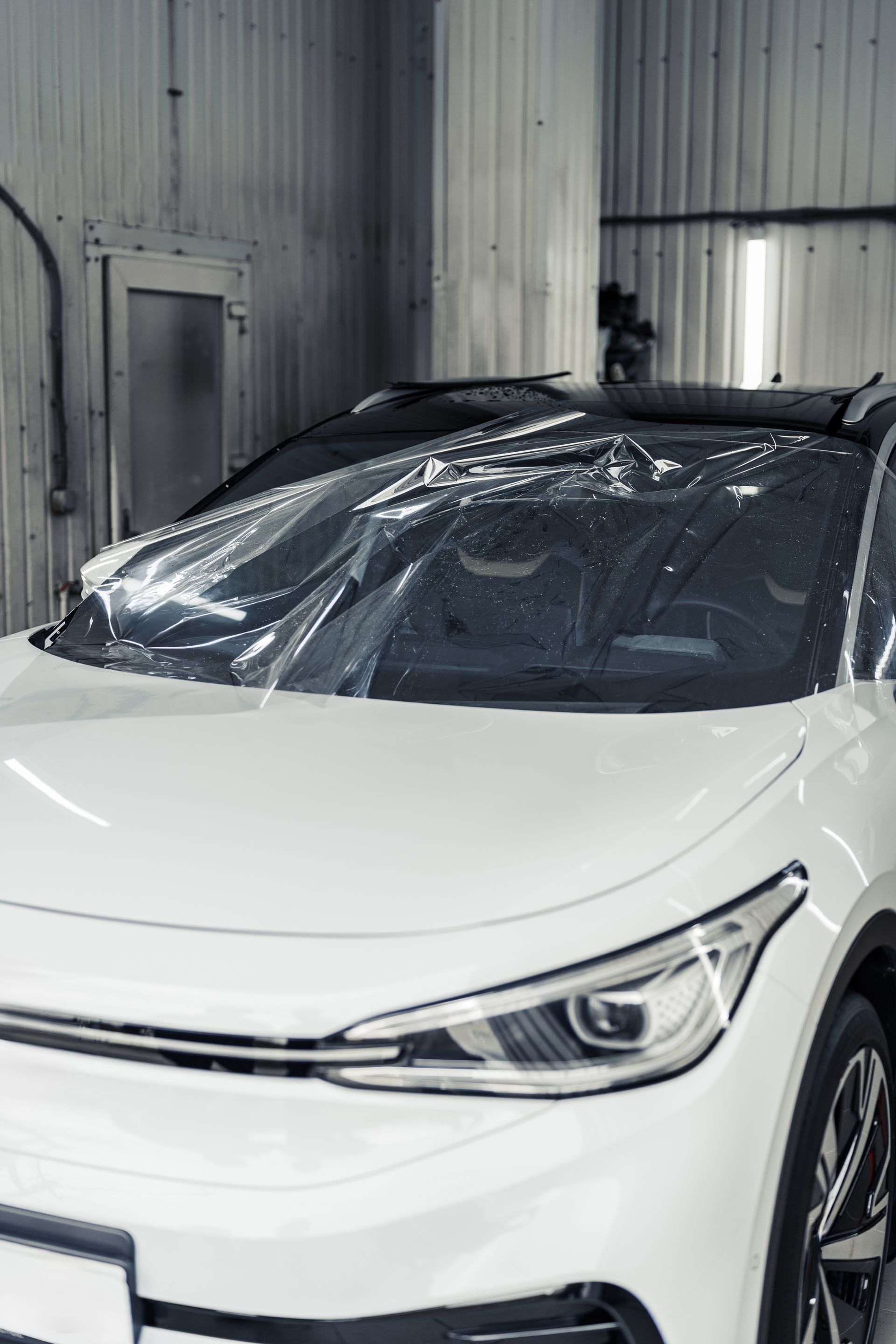 White car in a garage, covered with clear film on the windshield.