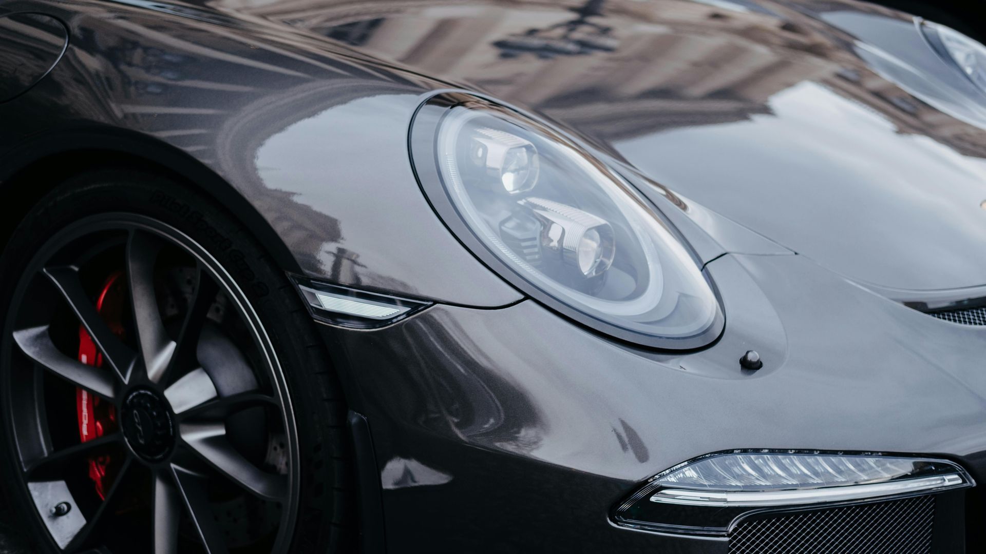 Person applying protective film to a gray car's hood, inside a garage.