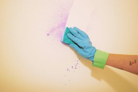 A person wearing gloves is cleaning a wall with a sponge.