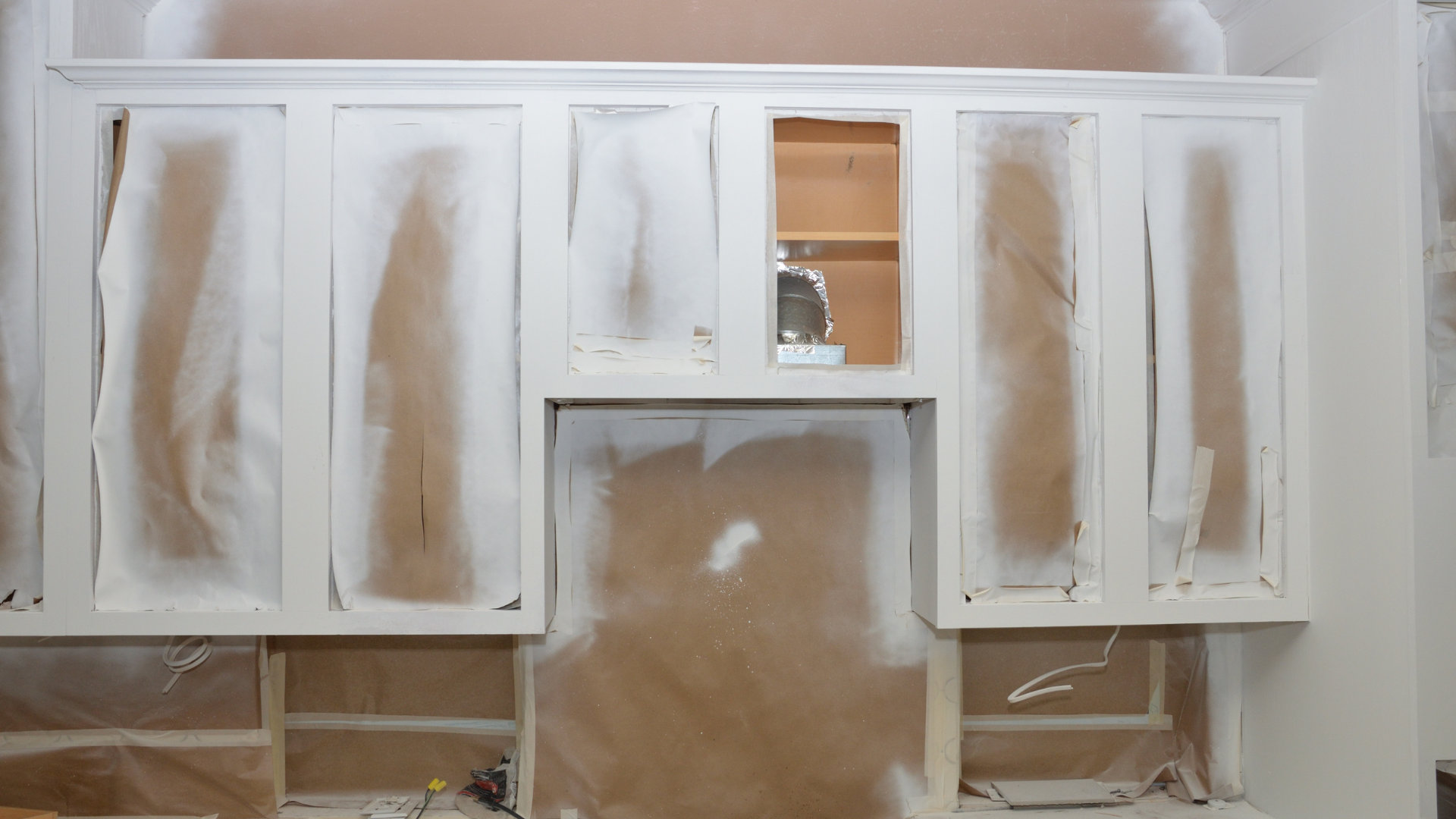 A kitchen cabinet is being painted white and is covered in plastic.