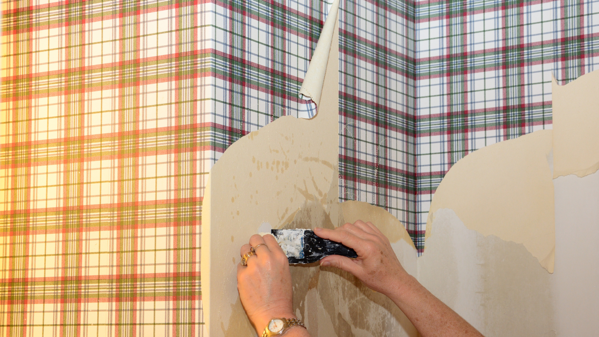 A person is removing wallpaper from a wall with a spatula.