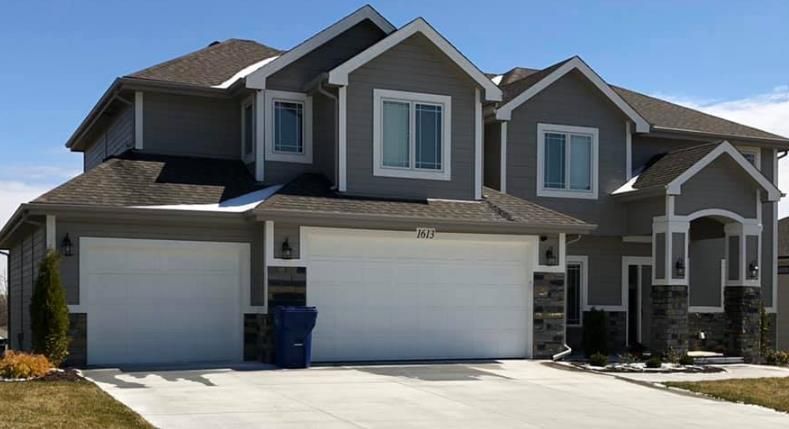 A large house with two garage doors and a blue trash can in front of it