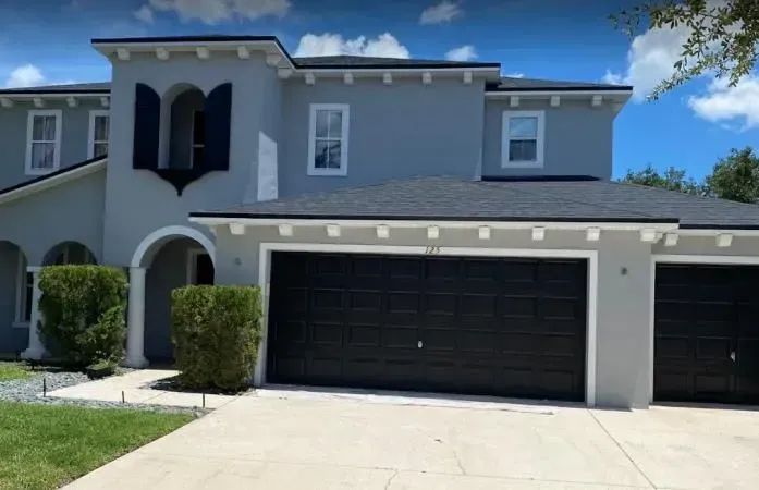 A large gray house with black garage doors and shutters on the windows.