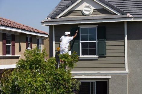 A man on a ladder is painting the side of a house