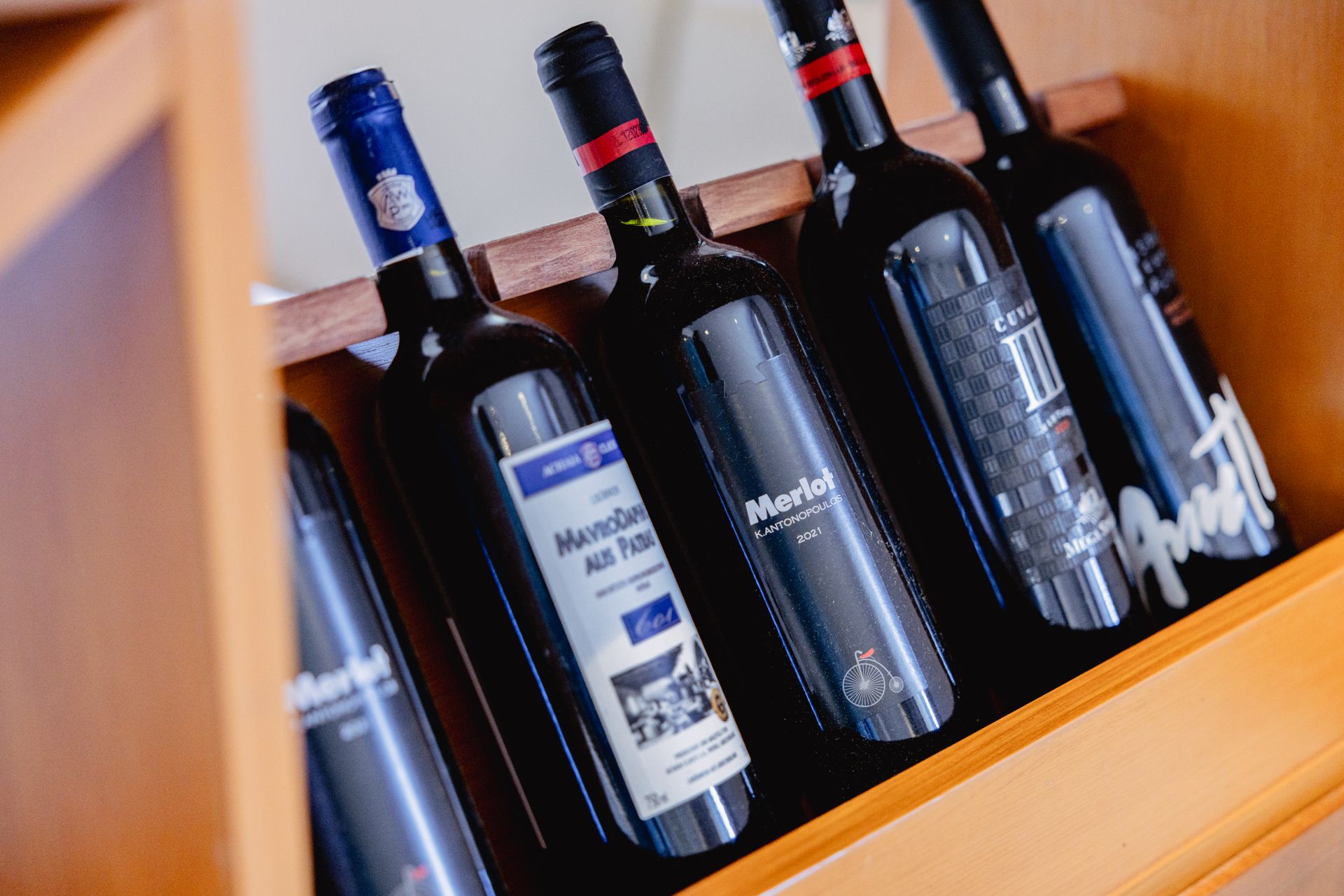 Weinflaschen im Holzregal; verschiedene Etiketten und Farben, Schrägansicht.