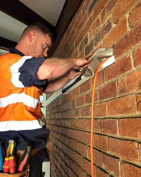 A Man in An Orange Vest Is Working on A Brick Wall — Paton's Electrical Services in Urangan, QLD