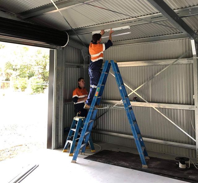 Two Men Are Working on A Ladder in A Garage — Paton's Electrical Services in Hervey Bay, QLD