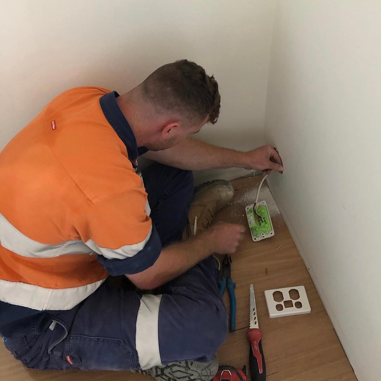 A Man Is Kneeling on The Floor Working on An Electrical Outle — Paton's Electrical Services in Craignish, QLD