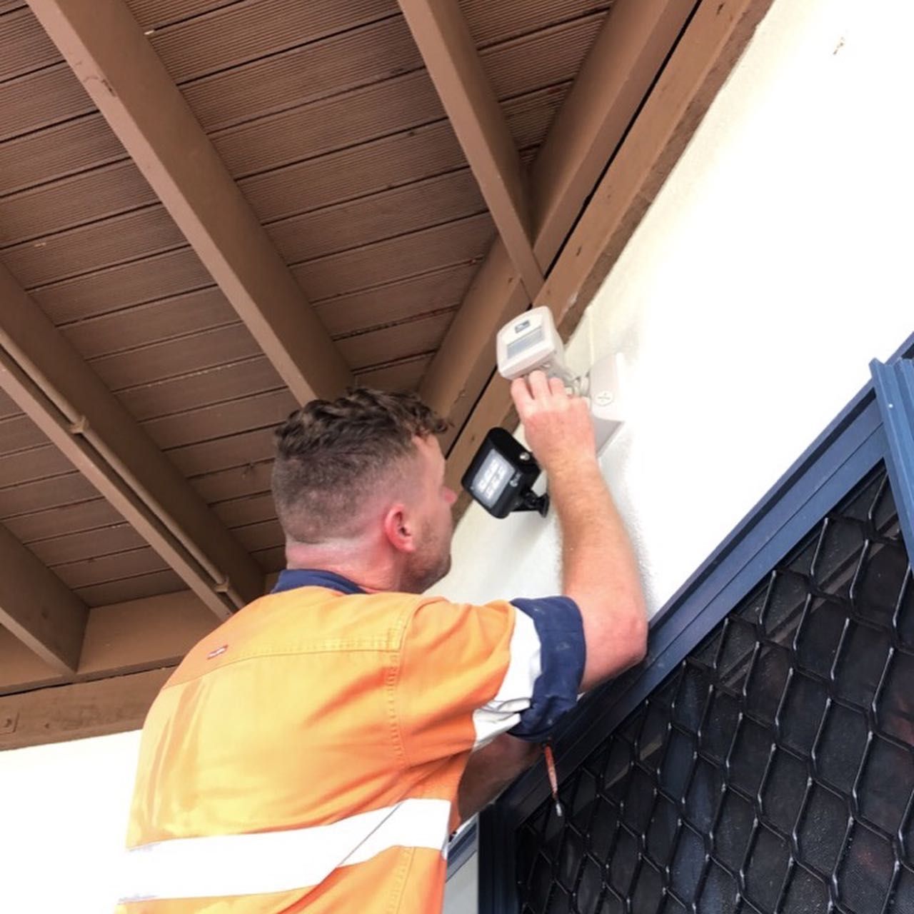 A Man in An Orange Shirt Is Working on A Light — Paton's Electrical Services in Hervey Bay, QLD