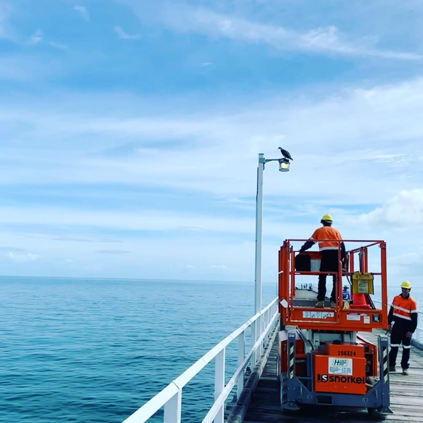 A Man Is Standing on A Lift on A Pier Overlooking the Ocean — Paton's Electrical Services in Hervey Bay, QLD