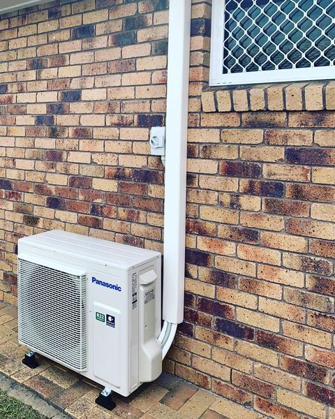 A White Air Conditioner Is Hanging on A White Wall — Paton's Electrical Services in Maryborough, QLD