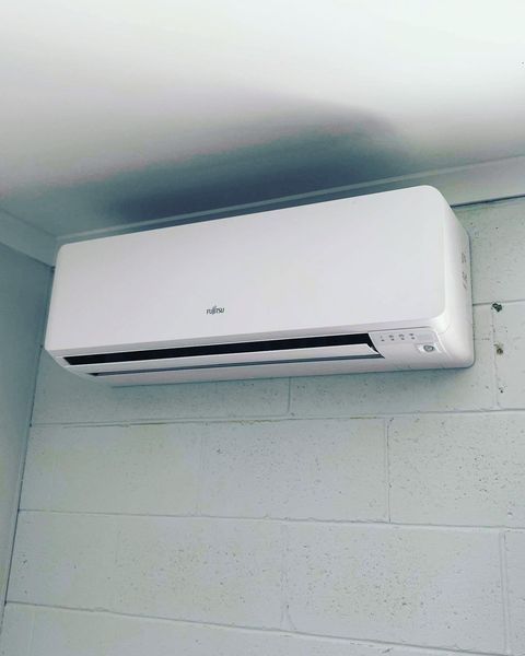 A White Air Conditioner Is Mounted on A White Brick Wall — Paton's Electrical Services in Urangan, QLD
